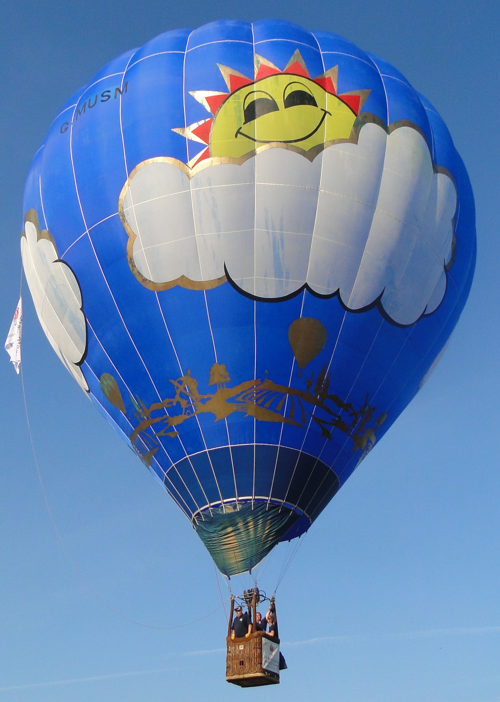 Blue balloon with a smiling sun peeping from behind a white cloud. Around the base of the balloon is a drawing in gold of a balloon flying over the countryside.